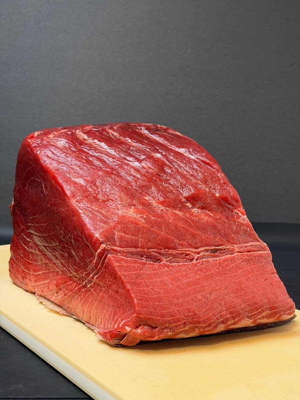A block of fresh bluefin tuna on a board, the grain in long curved lines