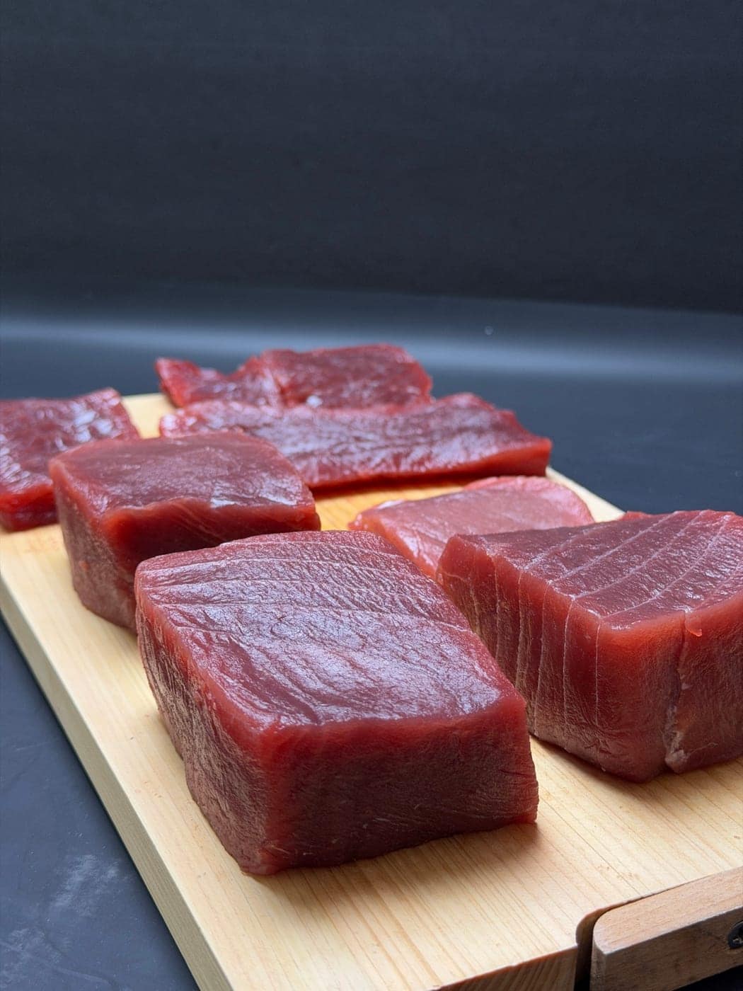 Blocks of bluefin tuna cut for selection on a wooden board, against a dark ground