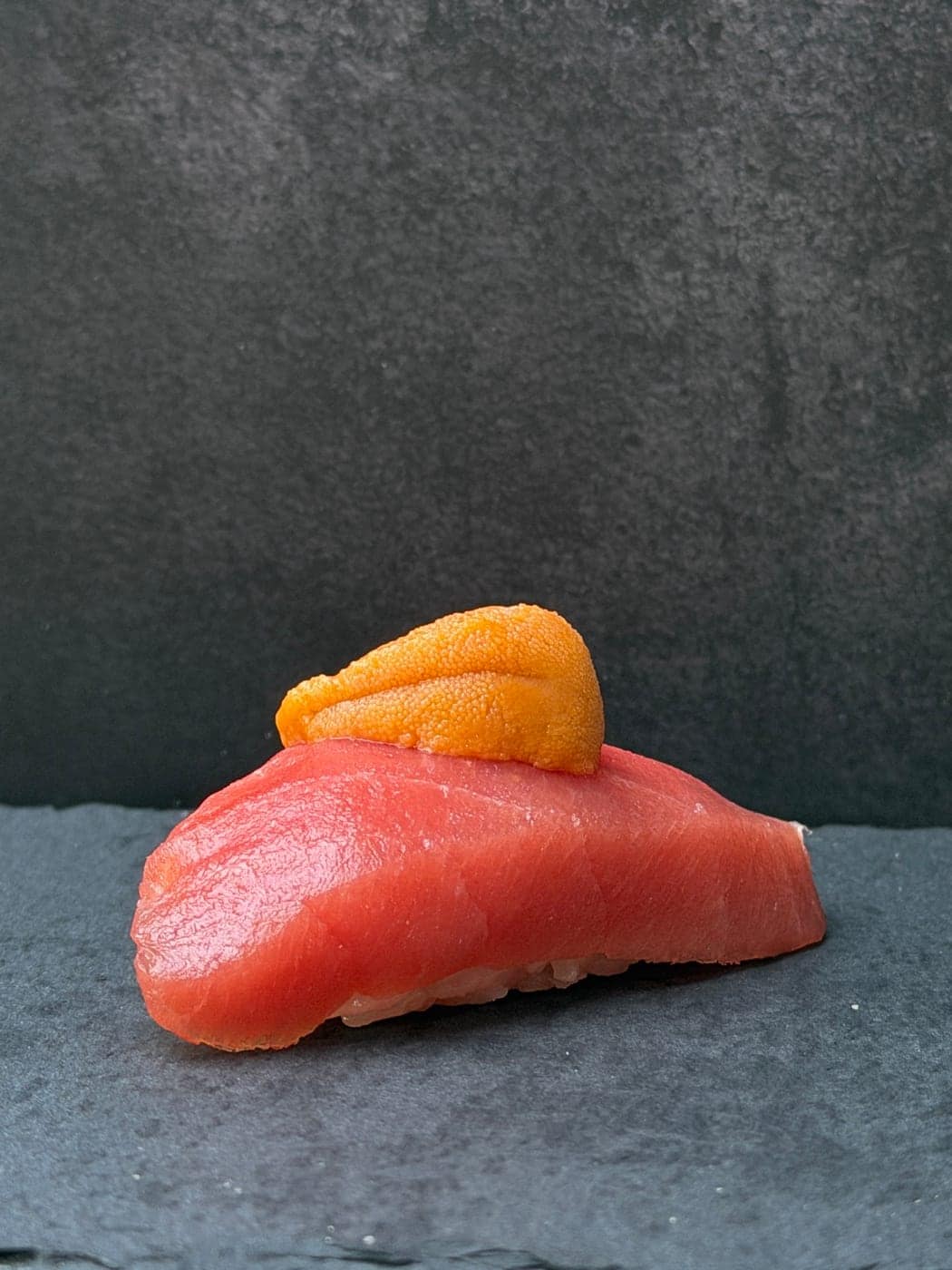A single piece of bluefin nigiri topped with a lobe of uni, on slate