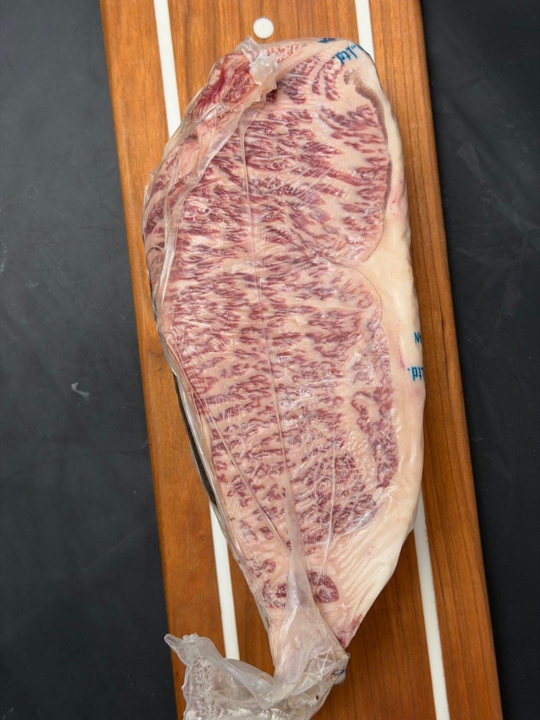 A whole Japanese A5 Wagyu strip loin, vacuum sealed, on a cherry board