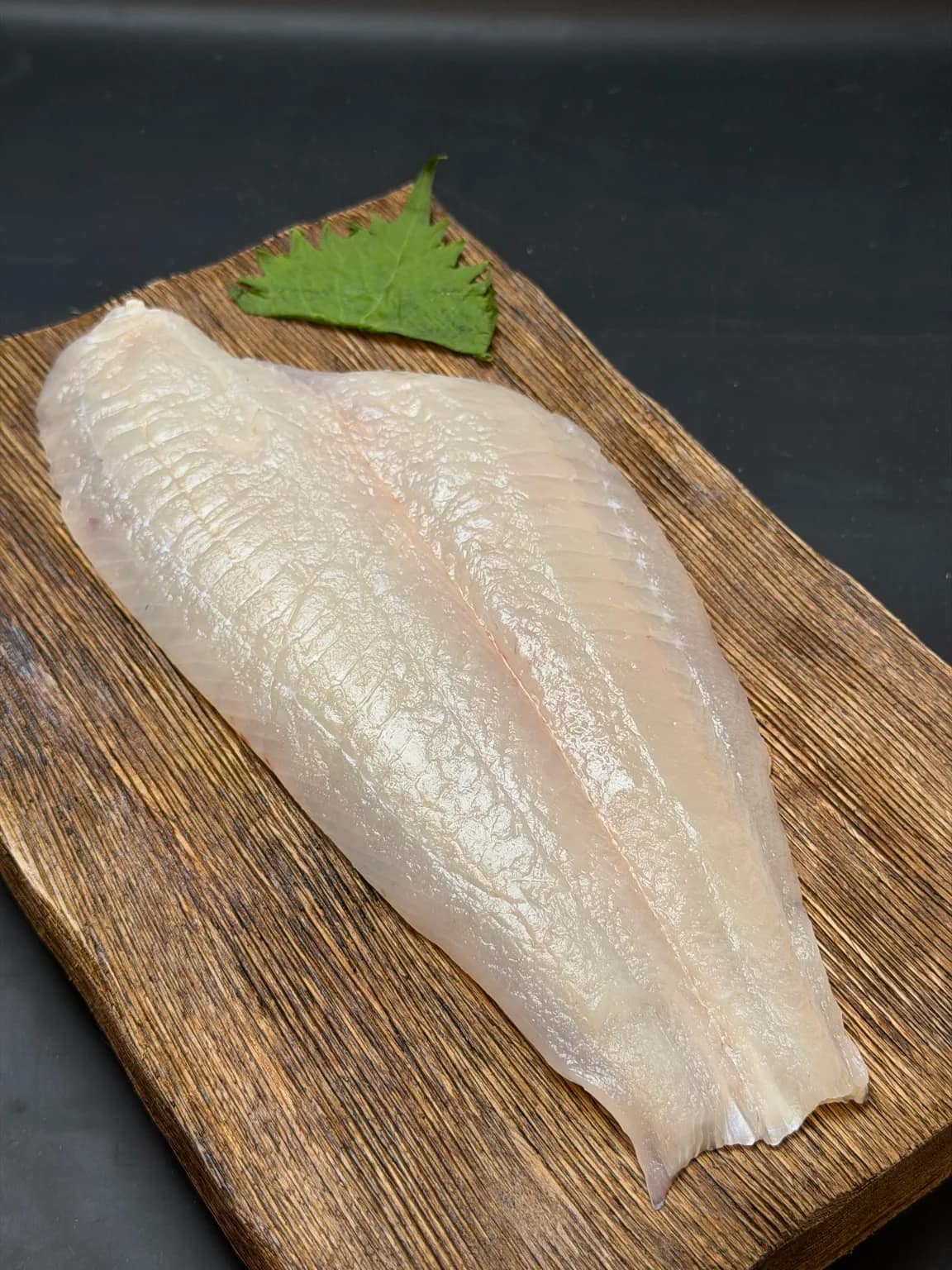 Fluke fillet on a wooden board with a green shiso leaf.