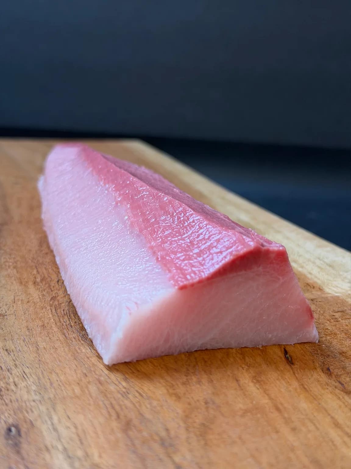 A portioned Japanese hamachi belly-side loin saku block on a wooden board.