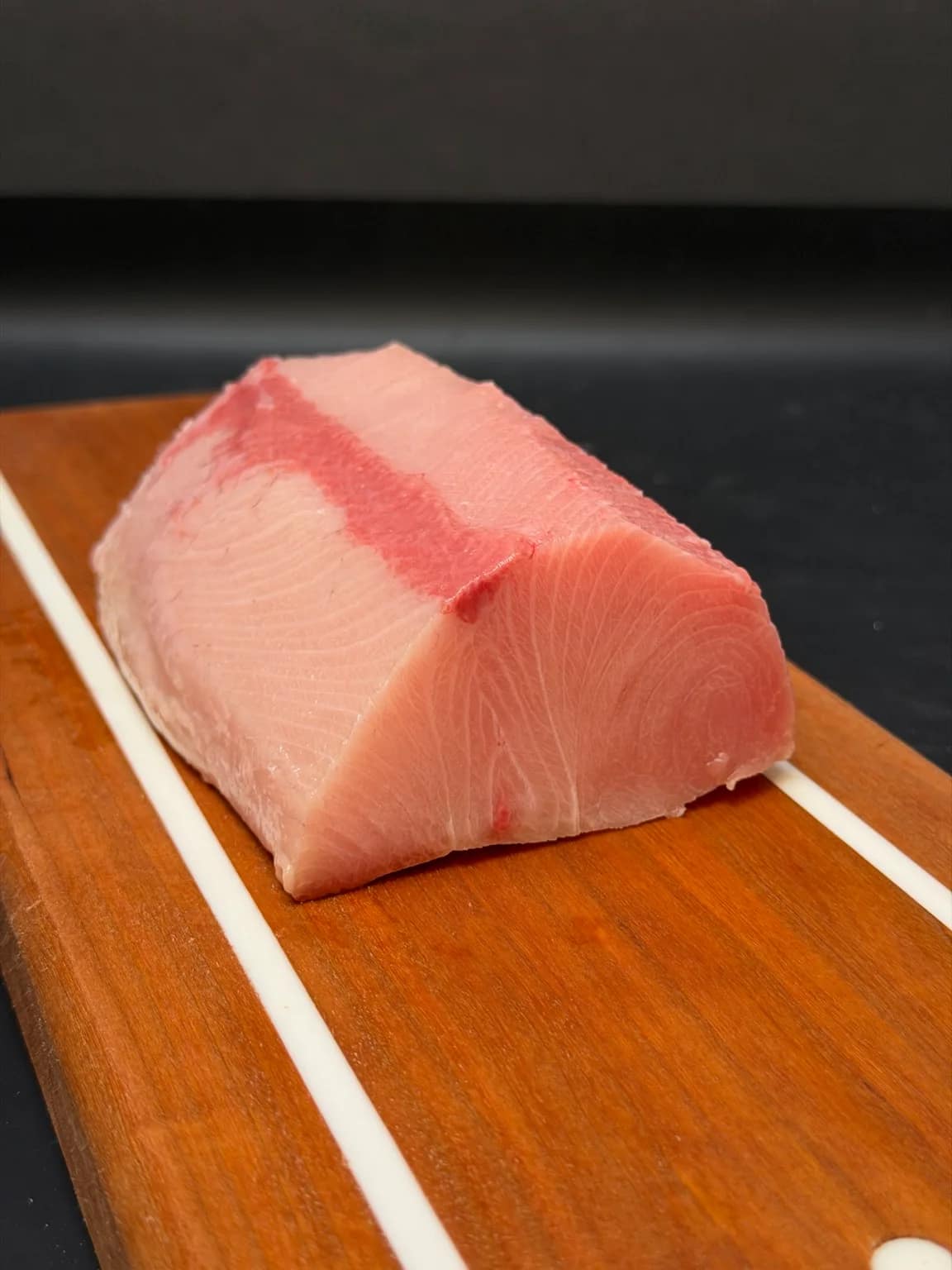 A portioned Japanese hamachi top-loin saku block on a wooden board, showing its cut face and natural marbling.