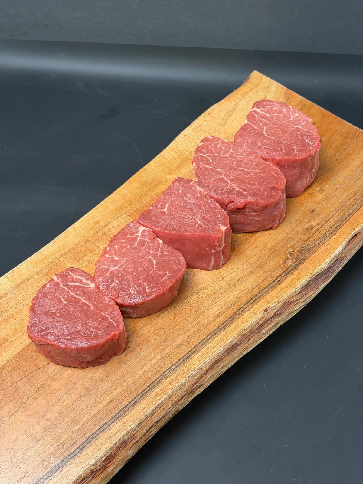 Thick-cut Angus filet mignon steaks arranged on a wooden board, showing their natural marbling.