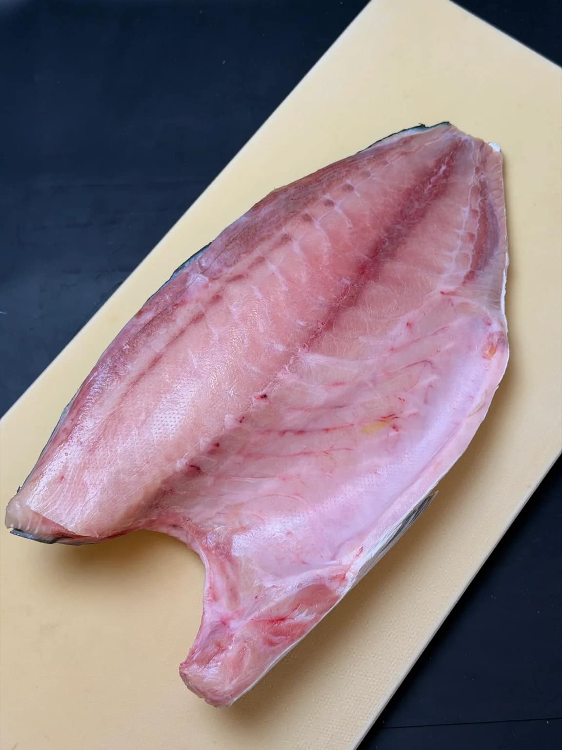 A whole Japanese hamachi fillet, flesh side up, on a cutting board.